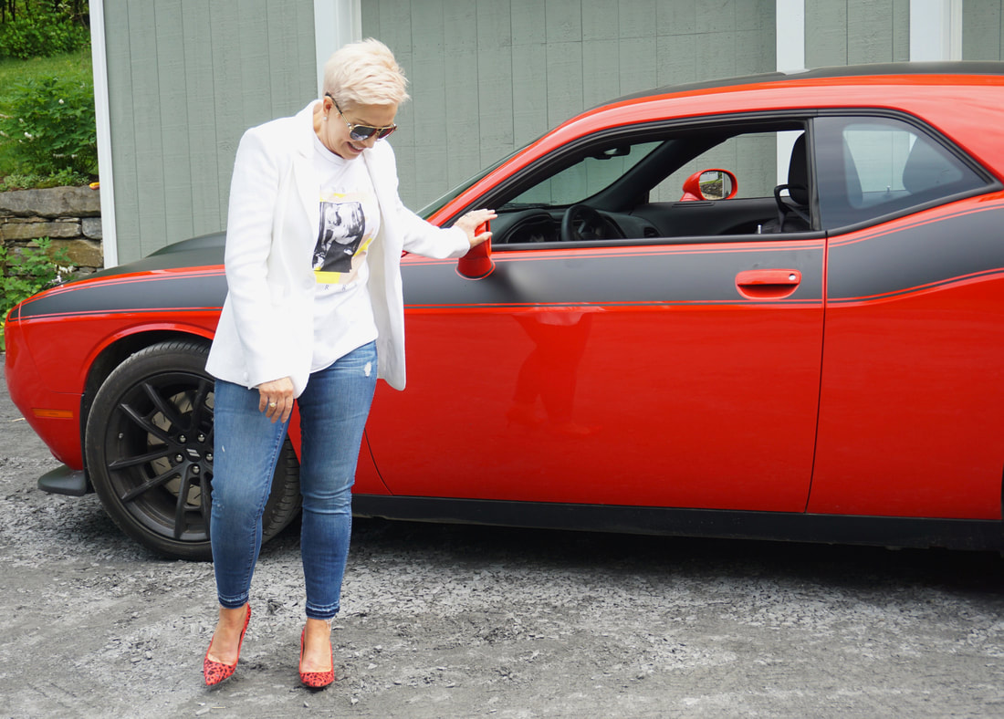 Mrs. Stafford in a white t-shirt & blazer, jeans & red high heels leaning against a red car