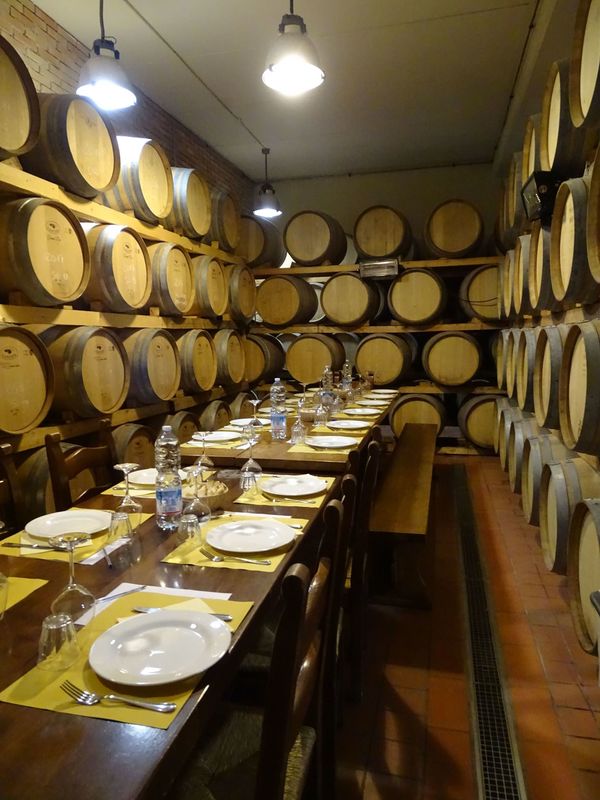 A dinner table set inside a winery adorned with wine barrels