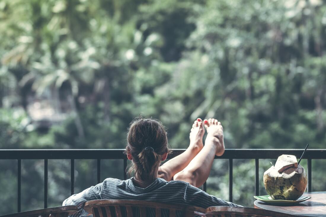 Woman relaxing with her feet up on the railing of her porch overlooking a tropical view