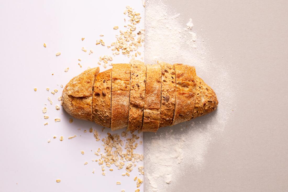 Loaf of bread sliced on a cutting board surrounded by loose oats