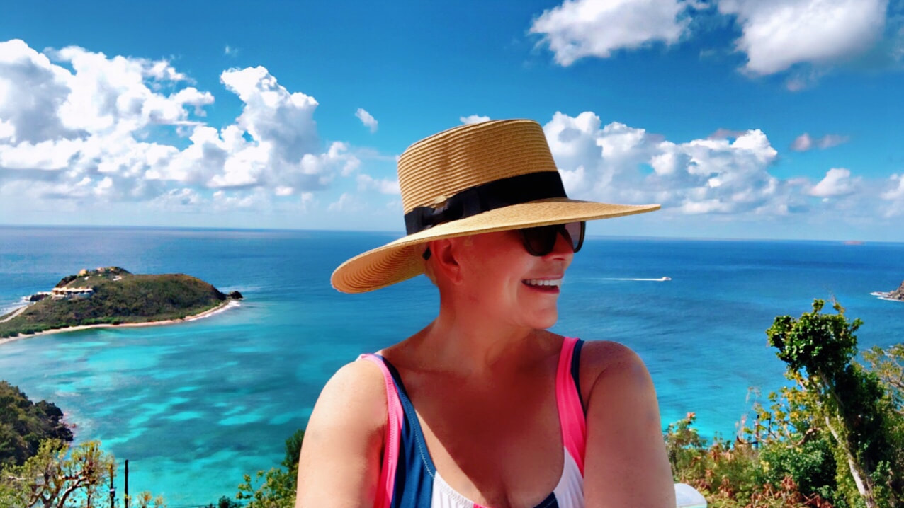 Mrs. Stafford in front of St. John landscape, laughing and wearing a sun hat