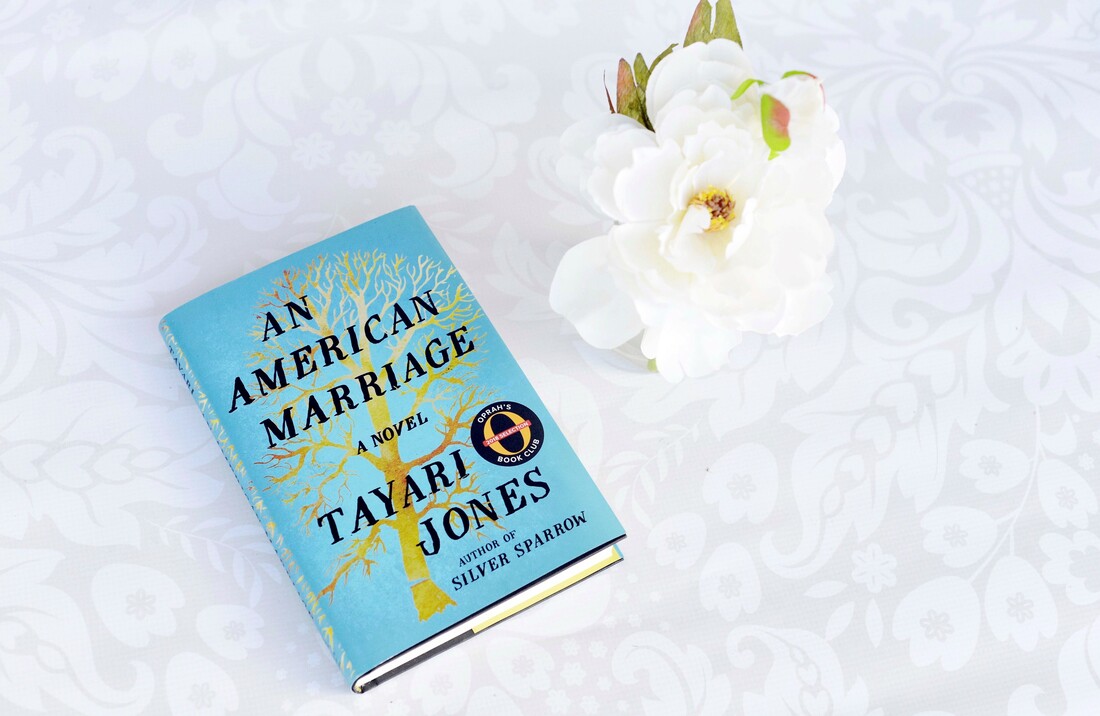 An American Marriage book on a table with white tablecloth and a white flower