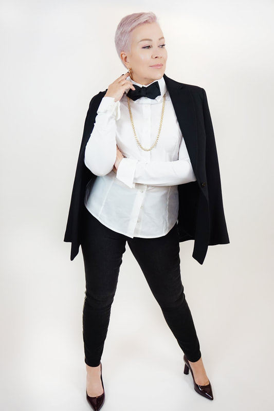 Mrs. Stafford poses in a black blazer, pants, heels & bowtie, with a white button-up and Gumuchian gold jewelry 